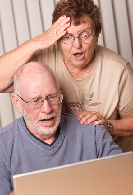Una pareja de adultos mayores sonrientes se divierten en la computadora
