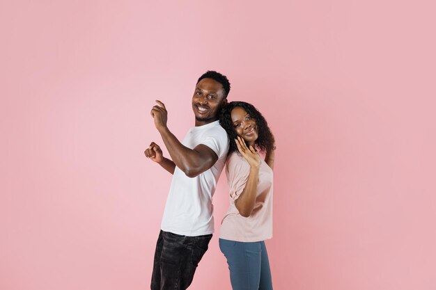Pareja africana de jóvenes divertidos y hombre y mujer bailando en el estudio sobre fondo de color rosa de moda