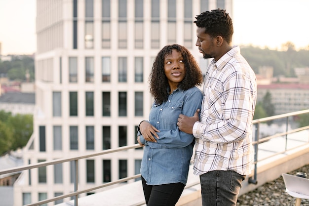 Una pareja africana, una mujer y un hombre, se abrazan en el techo de un edificio moderno.