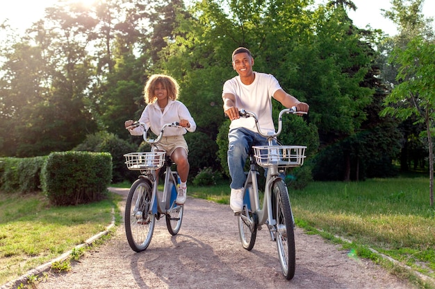 Una pareja afroamericana anda en bicicleta en el parque y habla hombre y mujer caminan en ecotransport