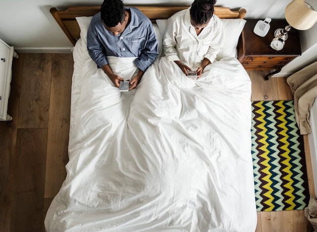 Pareja afroamericana en la cama usando teléfonos celulares