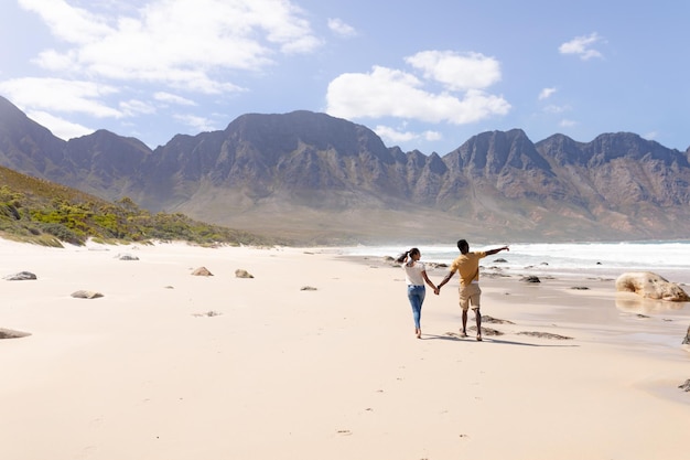 Pareja afroamericana caminando tomados de la mano en una playa junto al mar. estilo de vida saludable, ocio en la naturaleza.