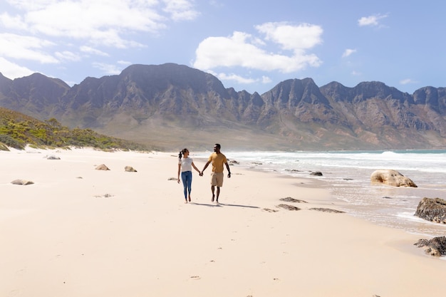 Pareja afroamericana caminando tomados de la mano en una playa junto al mar. estilo de vida saludable, ocio en la naturaleza.