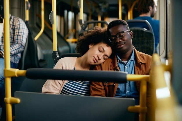 Pareja afroamericana cansada tomando una siesta mientras viaja en transporte público