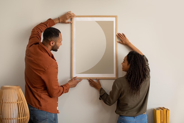 Pareja afroamericana colgando cartel en la pared en casa