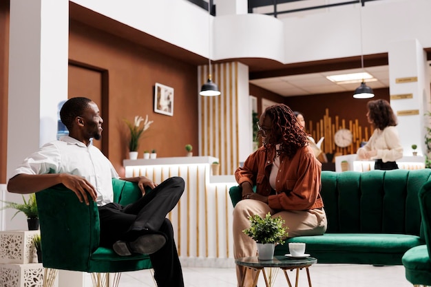 Una pareja afroamericana hablando en el vestíbulo, sentados en el salón del hotel y esperando registrarse en la recepción. Hombre y mujer felices llegando a un lujoso resort, relajándose en el sofá.