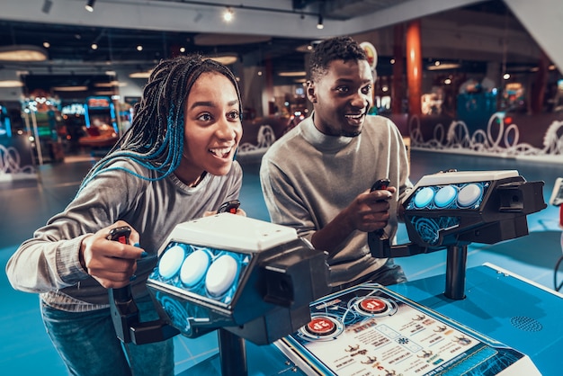 Pareja afroamericana pilotando naves espaciales azules en arcade.