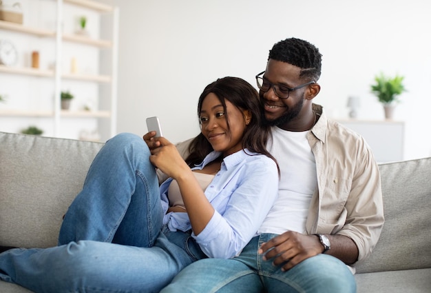 Pareja afroamericana sentada en el sofá usando un teléfono celular