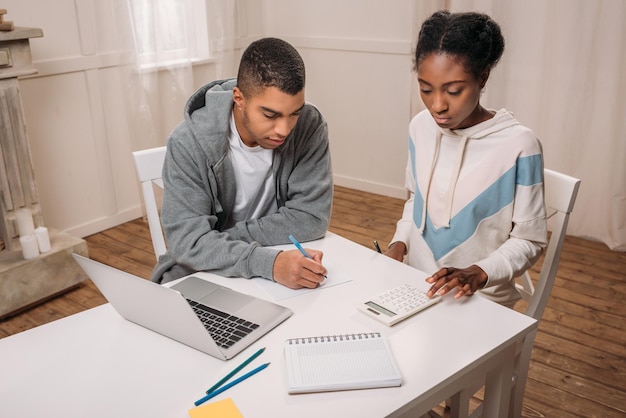 Pareja afroamericana seria con laptop calculando algo en casa