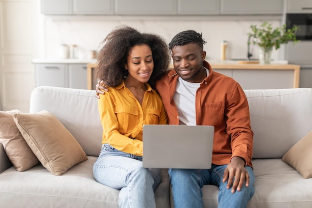 Una pareja afroamericana viendo una película en una computadora portátil en la sala de estar