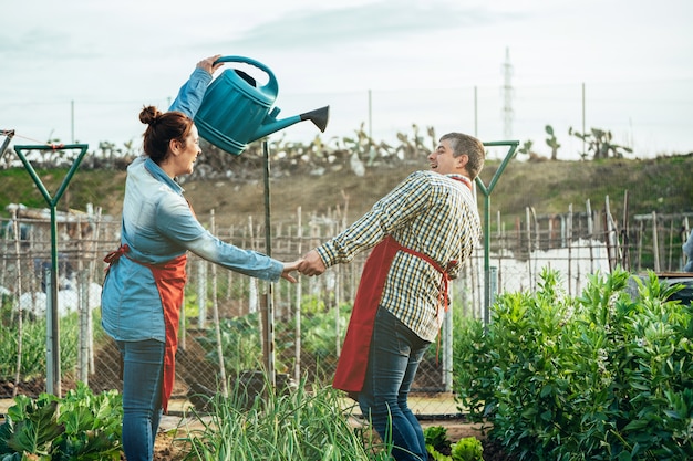 Pareja de agricultores sonriendo y jugando con una regadera en un campo orgánico