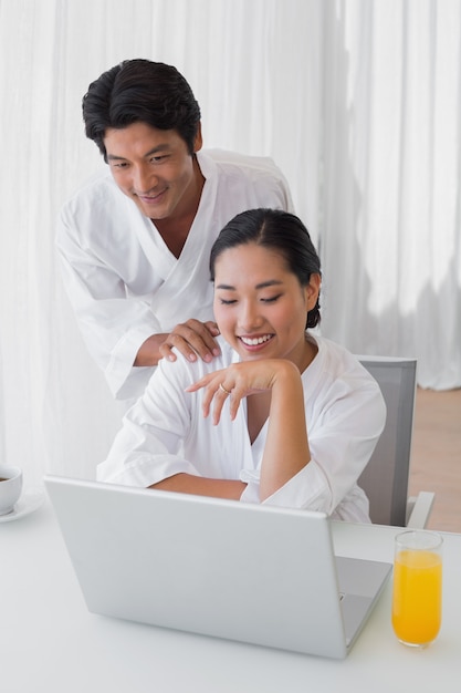 Pareja en albornoces usando laptop juntos en la mañana