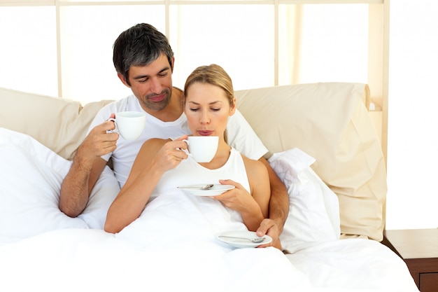 Pareja alegre bebiendo café acostado en la cama