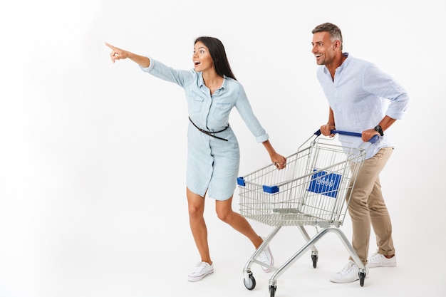 Pareja alegre corriendo con un carrito de compras