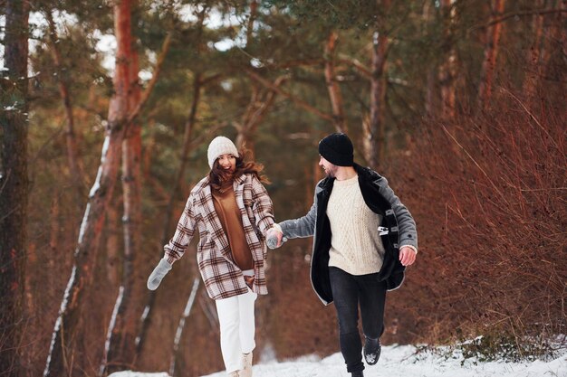 Una pareja alegre da un paseo por el bosque de invierno durante el día