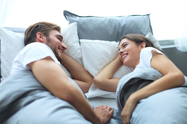 Pareja alegre despertando y mirando el uno al otro en la cama.