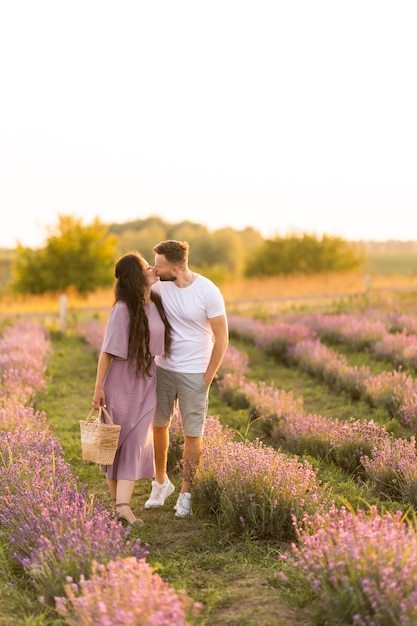 Una pareja alegre y elegante parada en el campo de lavanda sonriendo teniendo una cita romántica al atardecer