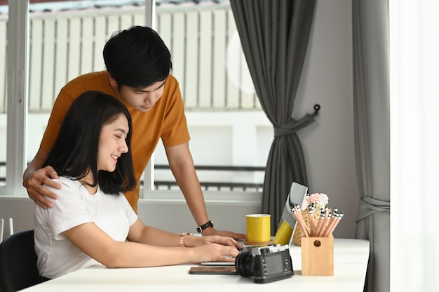 Una pareja alegre está usando una computadora portátil y descansando juntos en casa