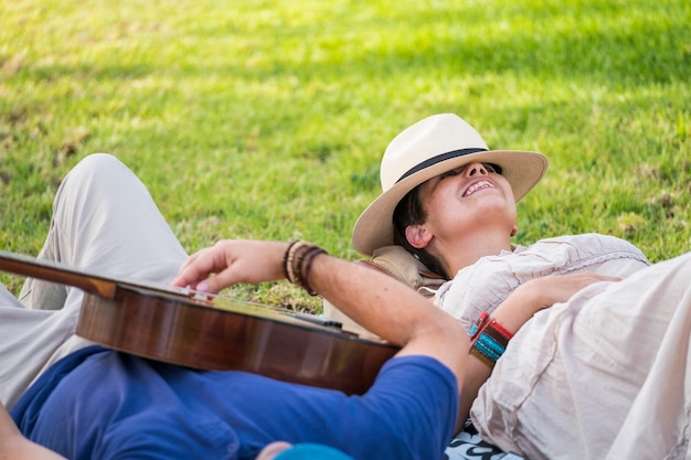 Pareja alegre feliz y relajada tumbada en el césped natural y disfrutar de la actividad de ocio al aire libre con un buen clima en la temporada de primavera el hombre toca una guitarra para la dama en concepto romántico