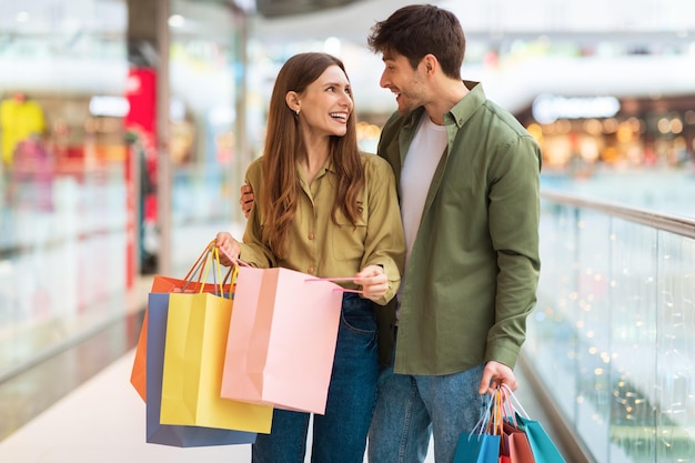 Pareja alegre haciendo compras sosteniendo coloridas bolsas de compras en el centro comercial