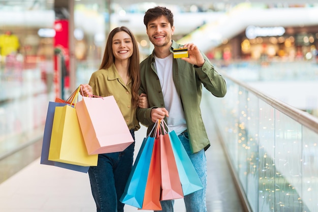 Una pareja alegre mostrando compras con tarjeta de crédito en un hipermercado moderno