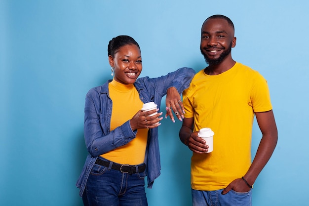 Una pareja alegre en una relación sosteniendo una taza de café en la mano. Jóvenes disfrutando de bebidas calientes, expresando sentimientos de amor y mirando a la cámara. Novia y novio en estudio.