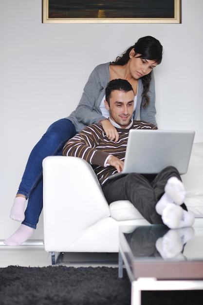 una pareja alegre se relaja y trabaja en una computadora portátil en la moderna sala de estar interior de la casa