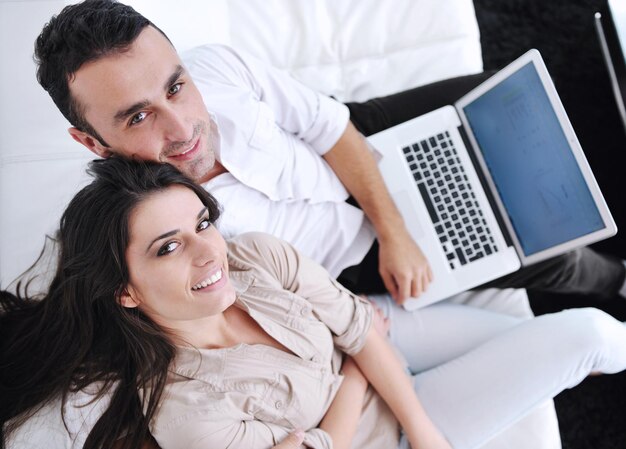 Foto una pareja alegre se relaja y trabaja en una computadora portátil en la moderna sala de estar interior de la casa