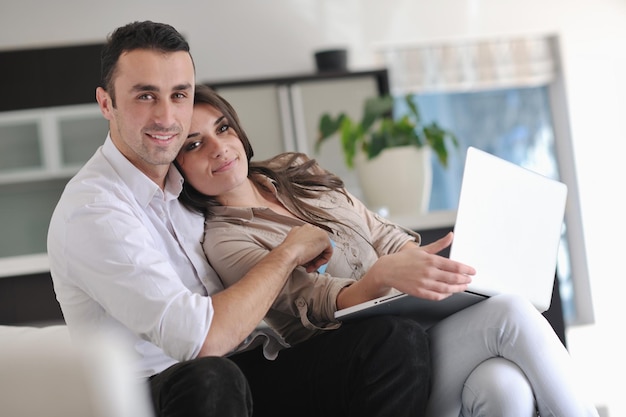 una pareja alegre se relaja y trabaja en una computadora portátil en la moderna sala de estar interior de la casa