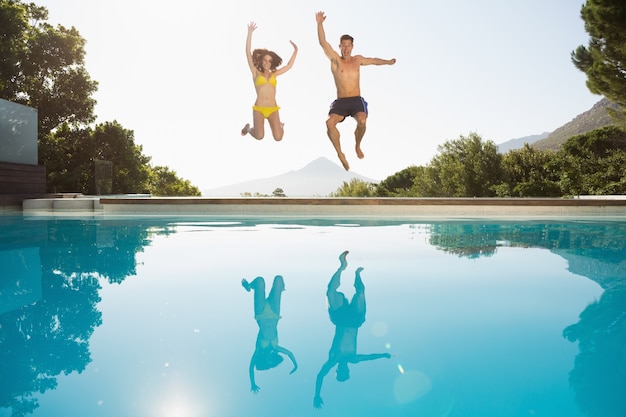 Foto pareja alegre saltando a la piscina