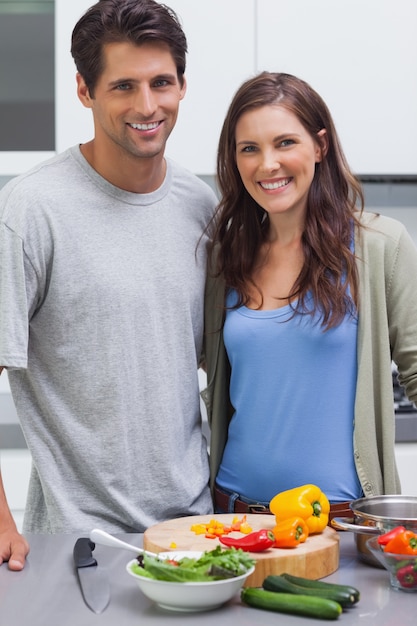 Pareja alegre sonriendo a la cámara y preparar verduras