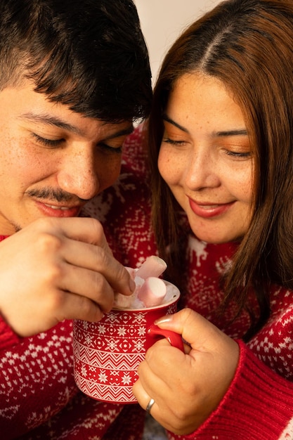 pareja alegre con sudadera de Navidad en la víspera de Navidad preparando un chocolate con malvaviscos
