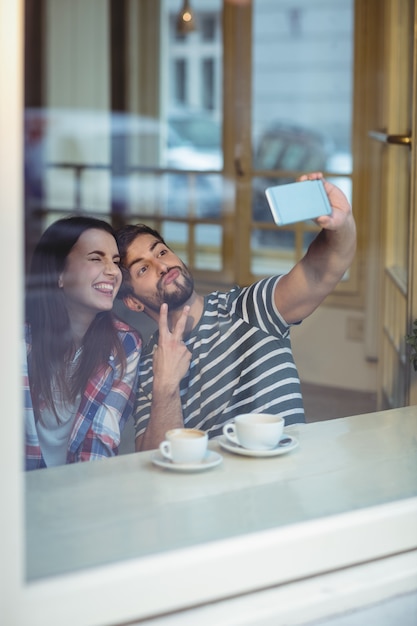 Pareja alegre tomando selfie en cafetería