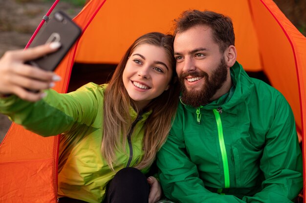 Pareja alegre tomando selfie durante el camping