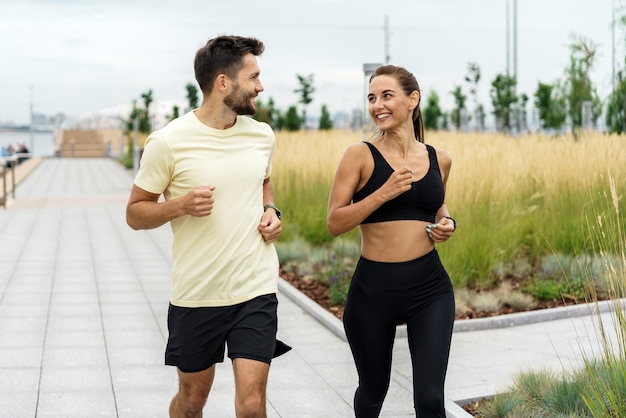 Una pareja alegre trotando juntos por un parque urbano rodeado de hierba alta y moderno