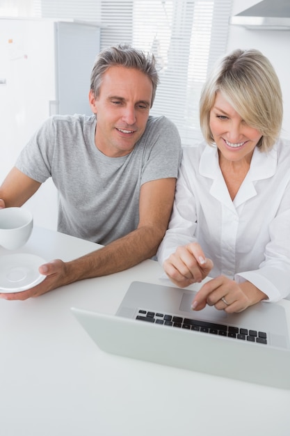 Pareja alegre usando la computadora portátil en la mañana