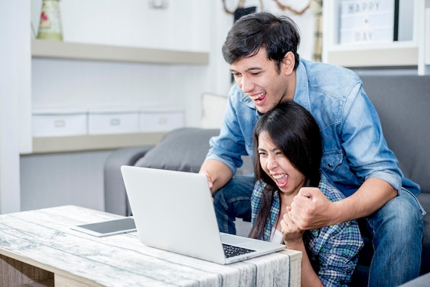 Una pareja alegre usando una computadora portátil mientras están sentados en casa