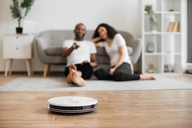 Pareja alegre viendo cómo el robot inalámbrico limpia la casa