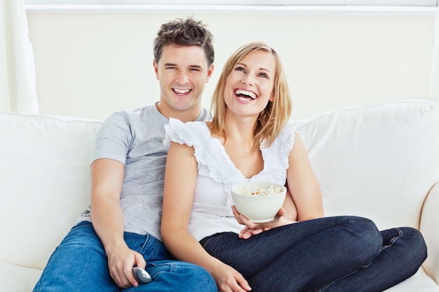 Pareja alegre viendo una película con pop-corn sentado en el sofá en la sala de estar