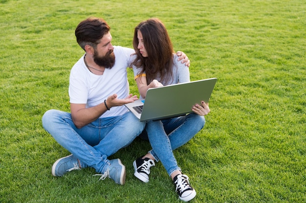 Una pareja alegre viendo una serie de portátiles al aire libre elige el concepto de película