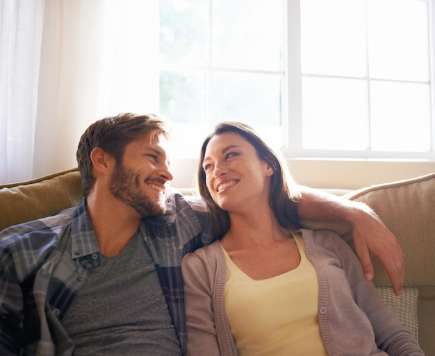 Pareja ama y abraza o sonríe el uno al otro en un sofá o en la sala de estar y conversación Hombre mujer y relación o vinculación y socios felices afectuosos o en casa relajándose y abrazando