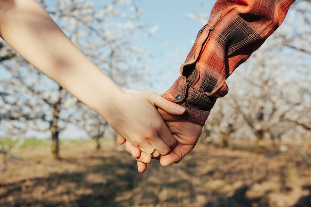 Foto pareja de amantes cogidos de la mano en un jardín floreciente de primavera. anillo en el dedo de la niña, compromiso.