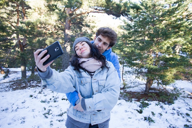 Pareja de amantes felices disfrutando en la nieve haciendo una selfie.