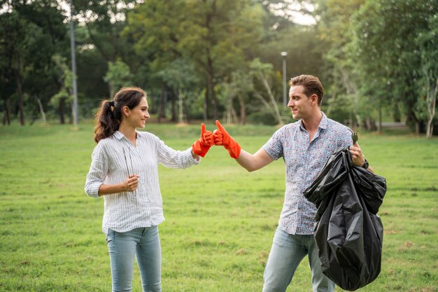 Pareja de amantes voluntarios que usan guantes caminando para recoger la basura en el parque Para mantener el medio ambiente limpio