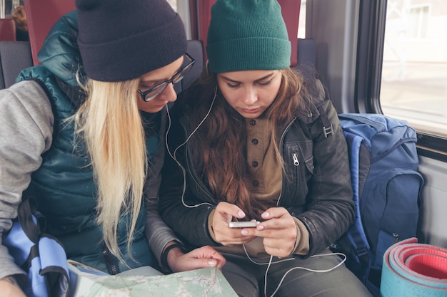 Pareja de amigas mirando el teléfono inteligente mientras está en el tren