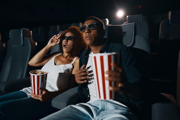 Una pareja de amigos enamorados viendo una película con palomitas de maíz en el cine.