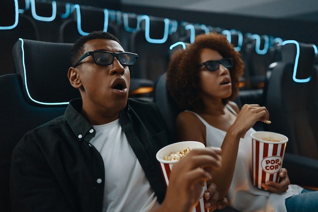 Una pareja de amigos enamorados viendo una película con palomitas de maíz en el cine.