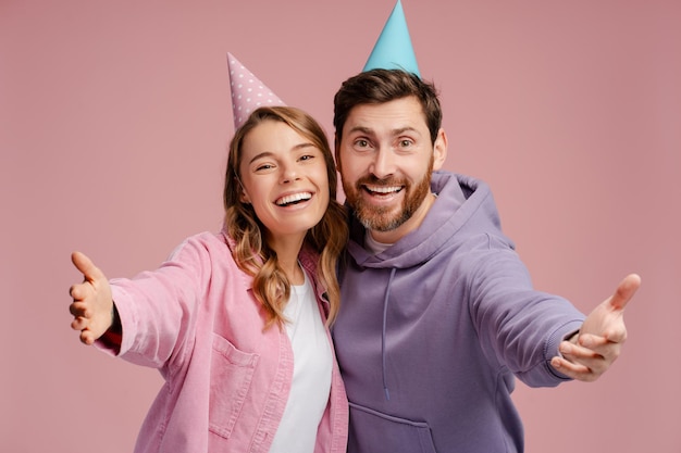 Una pareja de amigos felices con un cono de cumpleaños aislado en un fondo rosado.