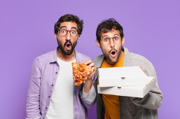 Pareja de amigos hispanos sorprendió expresión y sosteniendo pizzas para llevar