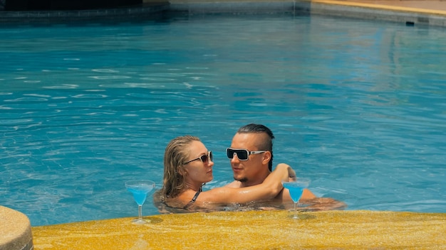 La pareja amorosa se abraza y besa bebiendo licor de alcohol de cóctel azul en la piscina